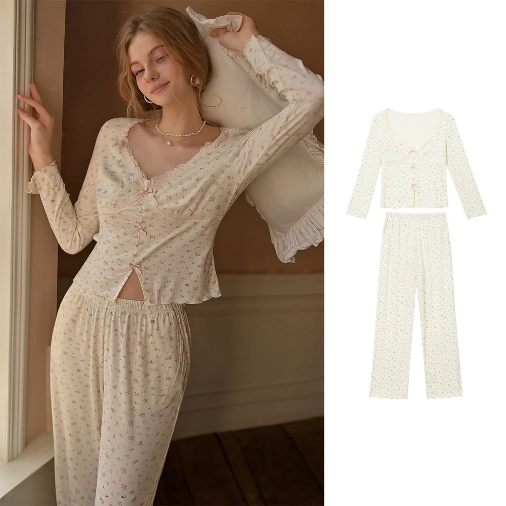 A two-piece pajama set shown on a model in a warm indoor setting on the left, and as a clean product flat-lay on the right. The set features a long-sleeve V-neck top and matching pants in a cream/off-white color with a tiny pink floral pattern.