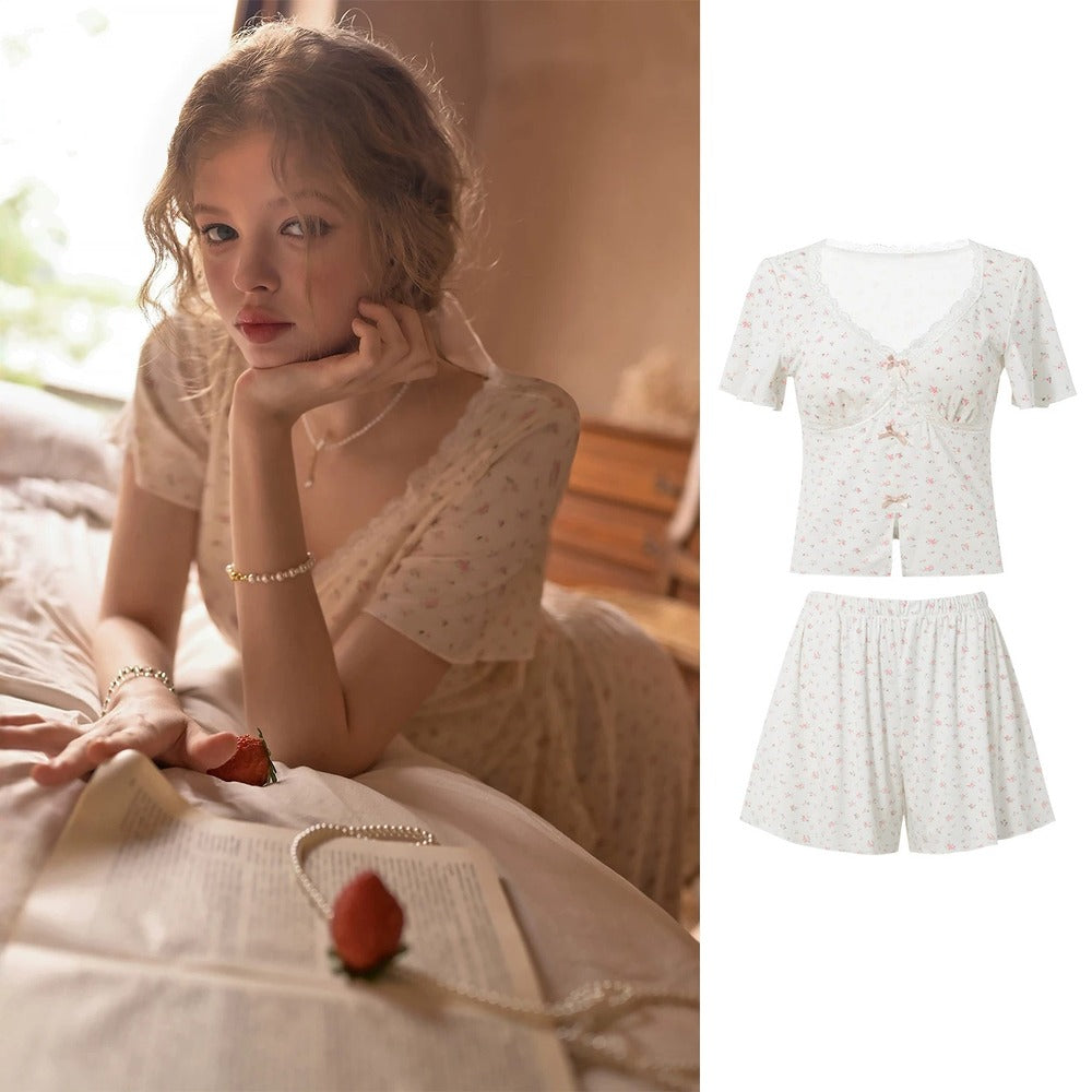 A woman reclines on a bed wearing a short-sleeve lace-up top and matching shorts set in a soft cream floral print. The left side shows her in a warm bedroom setting, while the right side shows a clean product composite of the matching two-piece outfit on a white background.