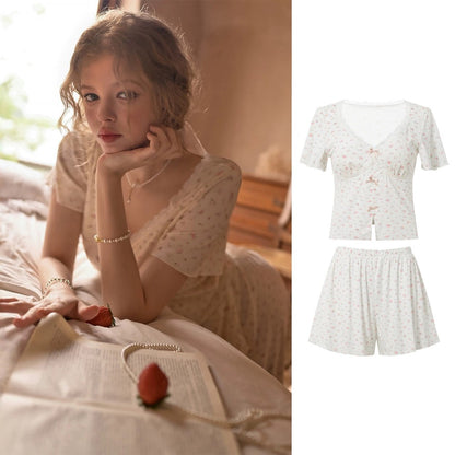 A woman reclines on a bed wearing a short-sleeve lace-up top and matching shorts set in a soft cream floral print. The left side shows her in a warm bedroom setting, while the right side shows a clean product composite of the matching two-piece outfit on a white background.