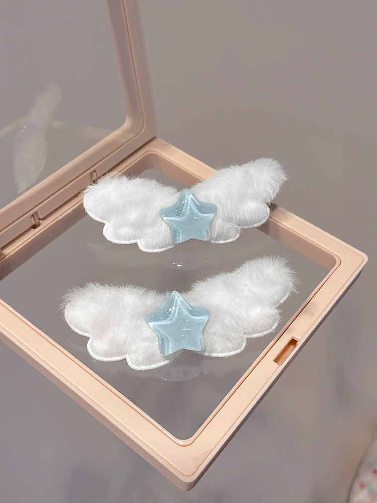 Two white fluffy angel wing hair clips with light blue star centers, displayed inside a clear-lidded beige makeup compact.