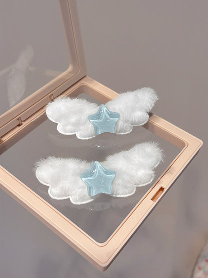 Two white fluffy angel wing hair clips with light blue star centers, displayed inside a clear-lidded beige makeup compact.