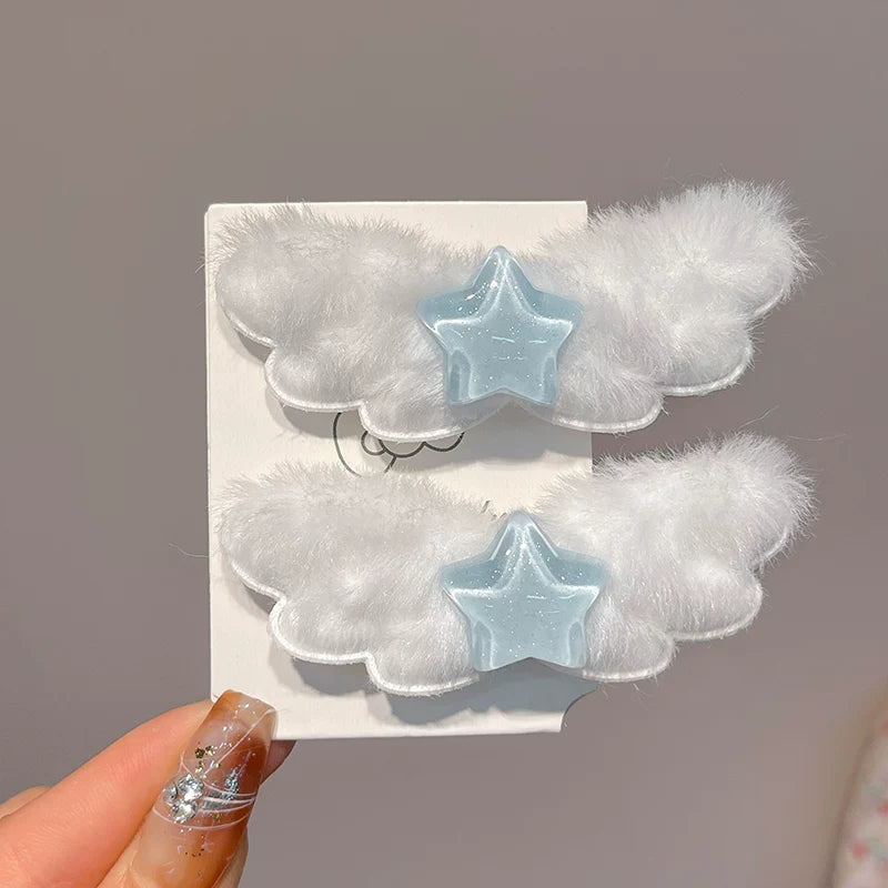 Two white fluffy cloud-shaped hair clips with light blue star centers, displayed on a white card held by a hand with glittery nail polish against a soft gray background.
