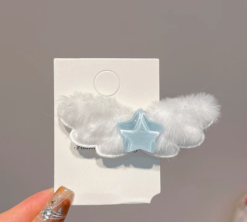 A white fluffy cloud-shaped hair clip with a light blue star in the center, displayed on a white card with a hand holding the corner.
