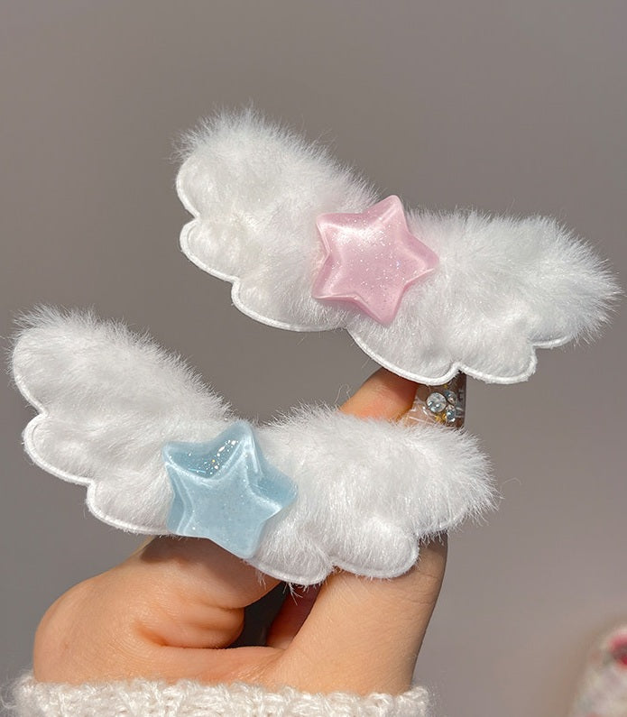 Two white fluffy cloud-shaped hair clips with star accents, one pink and one light blue, held in a hand against a soft gray background.