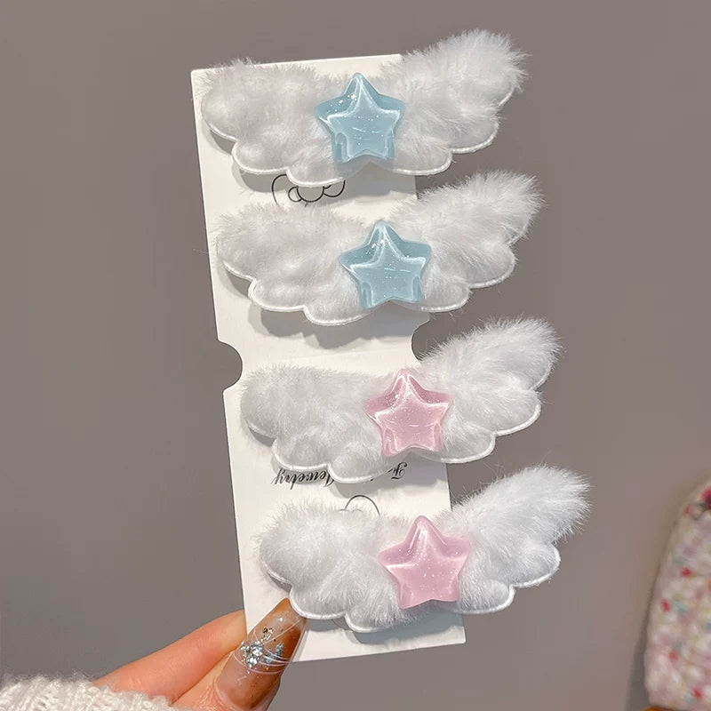 Four white fluffy angel-wing hair clips with star accents in light blue, dark blue, pink, and light pink, displayed on a white card held by a hand.