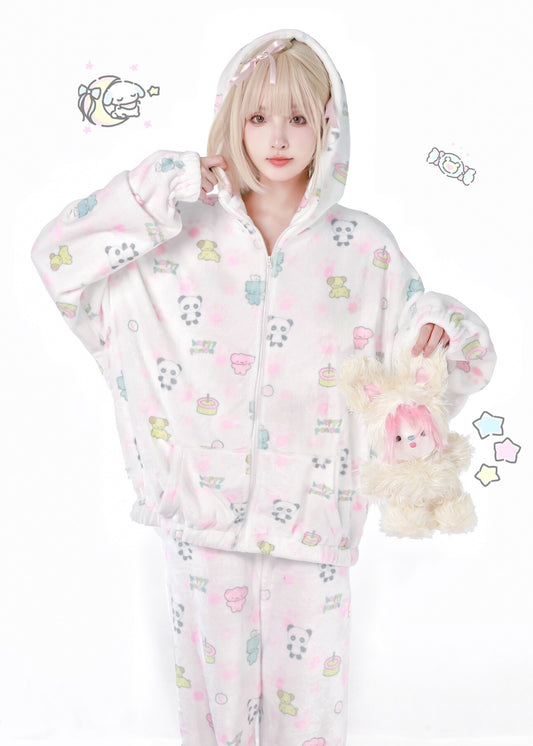 A model wearing a light pink and white hooded fleece pajama set with a cute pastel cartoon print, holding a plush toy against a white background.