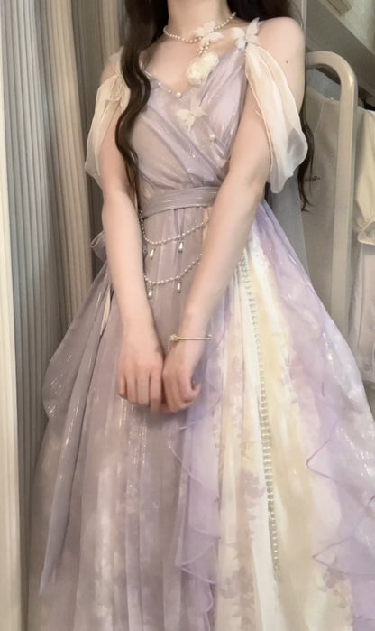 A woman wearing a lavender and cream tulle ball gown with sheer draped sleeves, a matching waist belt, and delicate pearl-like chain accents, photographed indoors.