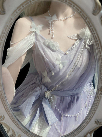 A close-up of a person wearing a pale lavender and white sheer dress with floral appliqués, pearl necklaces, and delicate chain details, framed by an ornate oval mirror.