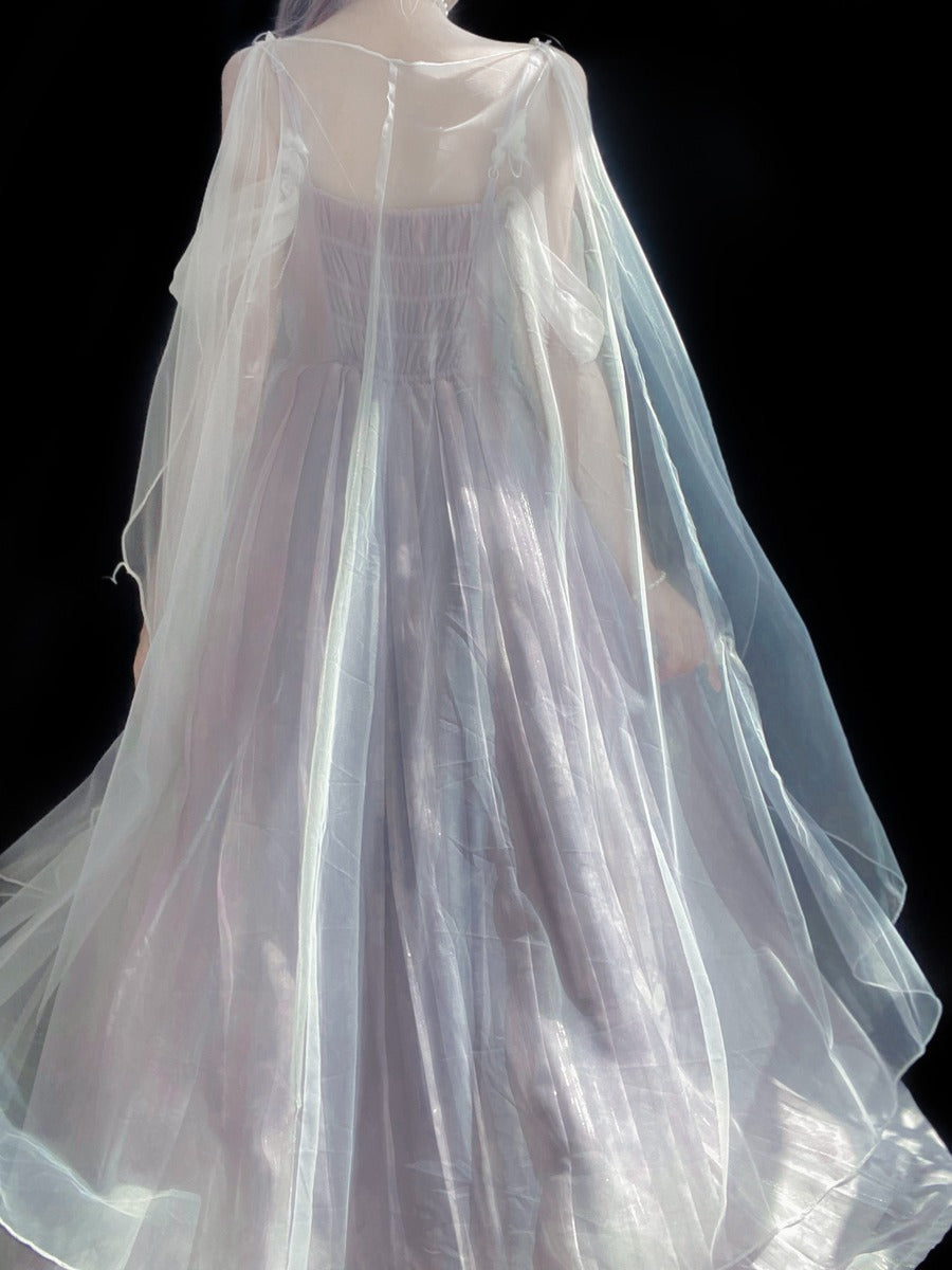 A sheer white tulle cape or drape worn over a long, light lavender dress, shown from the back against a solid black background.