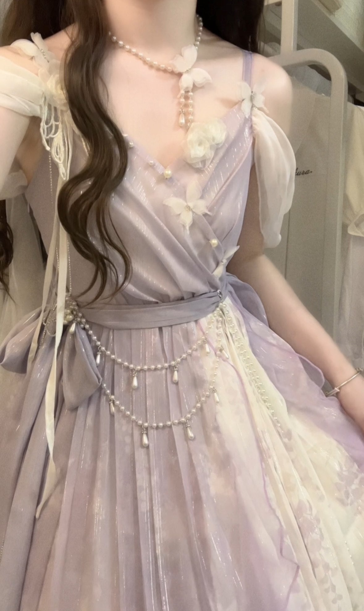 A close-up of a person wearing a lavender and white Lolita-style dress with pearl necklaces and floral details.