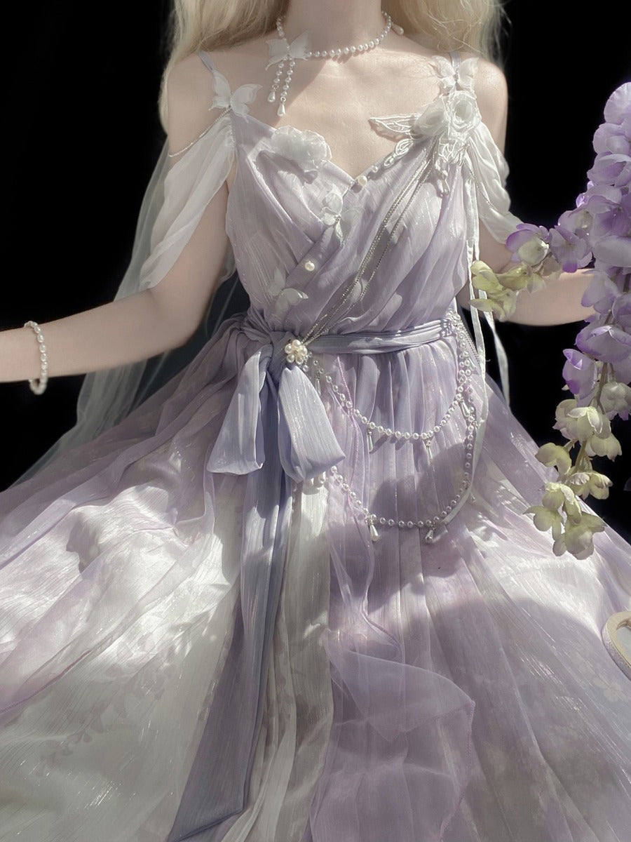 A close-up of a doll or mannequin wearing an ornate lavender and white tulle dress with pearl-like bead details, shown against a black background with purple flowers at the side.
