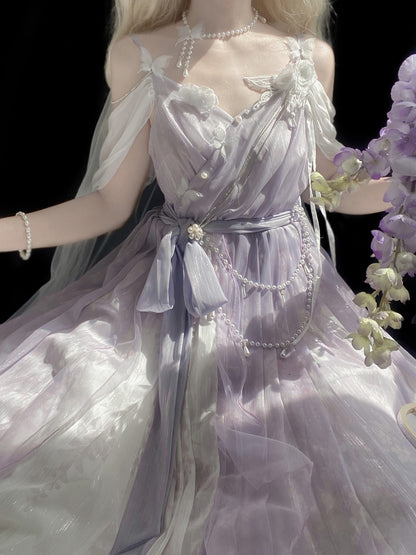 A close-up of a doll or mannequin wearing an ornate lavender and white tulle dress with pearl-like bead details, shown against a black background with purple flowers at the side.