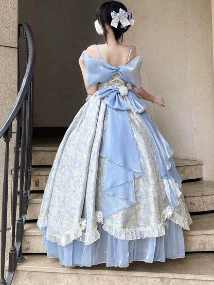 A woman stands on stone steps wearing a voluminous light blue ball gown with a large bow at the back, ruffled layers, and a pale floral pattern. She has her hair up with a large bow accessory.