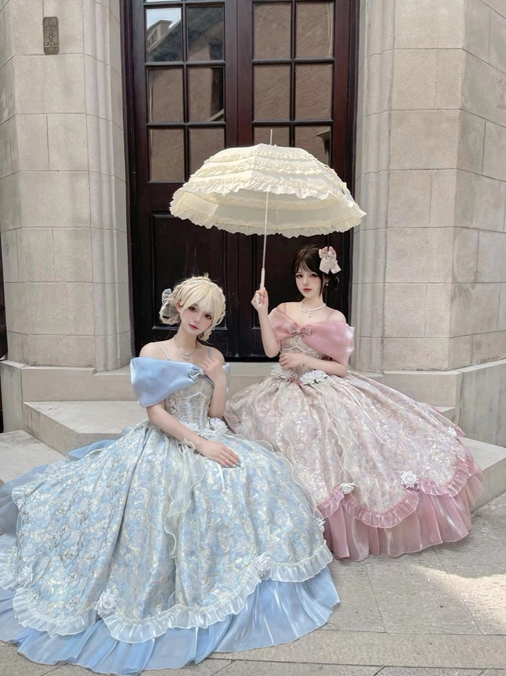 Two women in elaborate historical-style ball gowns pose on stone steps in front of a dark wooden door. One wears a light blue off-the-shoulder lace gown and holds a cream lace parasol, while the other wears a pink off-the-shoulder lace gown.