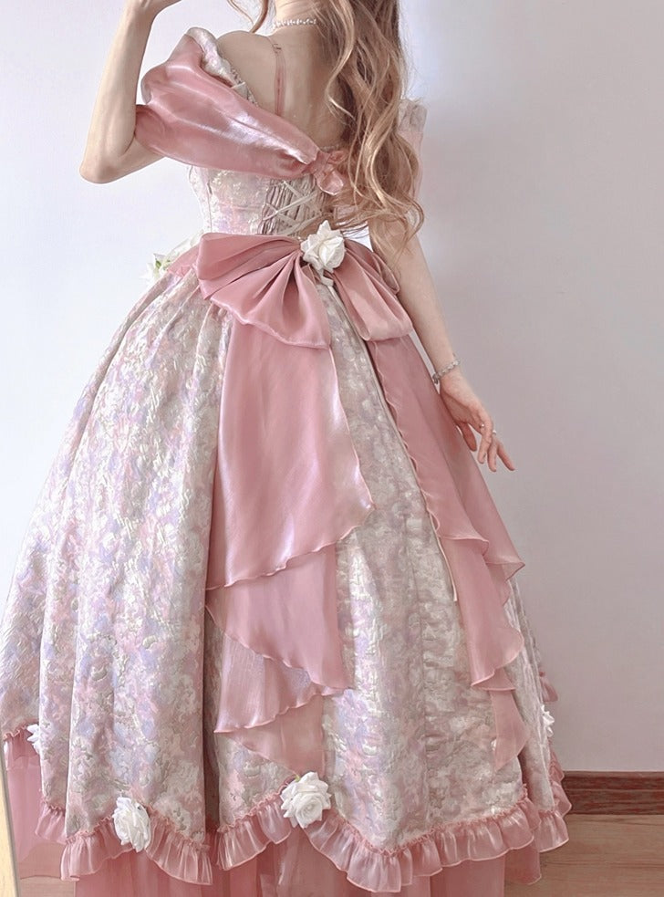 A woman wearing a voluminous pastel pink and white Lolita-style ball gown with layered ruffles, a large bow at the back, and floral fabric details.