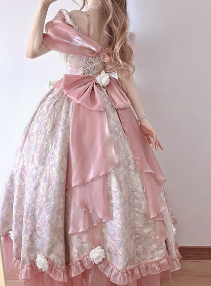 A woman wearing a voluminous pastel pink and white Lolita-style ball gown with layered ruffles, a large bow at the back, and floral fabric details.