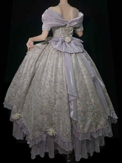 A voluminous off-the-shoulder ball gown with a lavender satin bow and a heavily embroidered beige lace overlay, shown from the back against a black background.