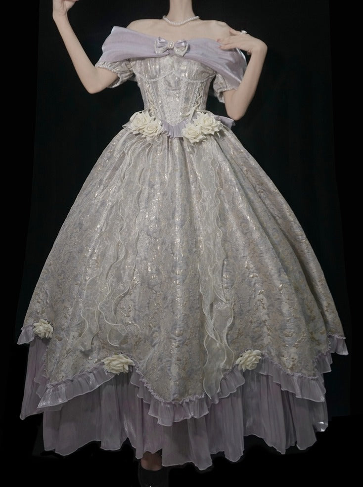 A voluminous off-the-shoulder ball gown with a heavily embroidered bodice, floral appliqués at the waist and hem, and layered ruffled tulle in a pale lavender and champagne tone, shown against a black background.