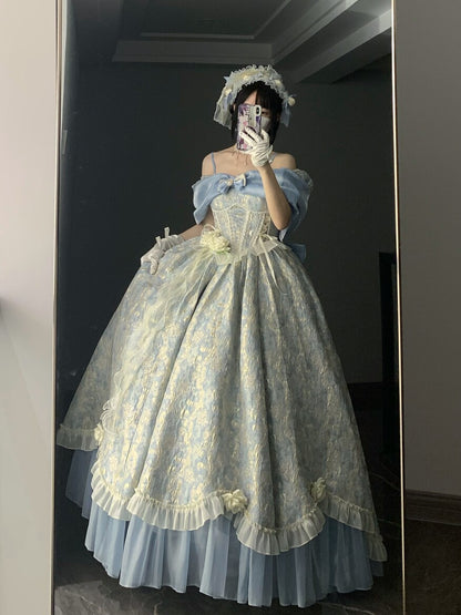 A person takes a mirror selfie wearing an elaborate off-the-shoulder ball gown in pale blue and cream lace, with matching gloves and a floral headpiece in a dark indoor room.