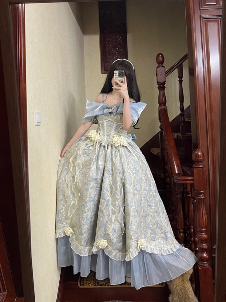 A woman takes a mirror selfie wearing an elaborate off-the-shoulder ball gown with a light blue and beige damask pattern, set in an indoor hallway with a wooden staircase.