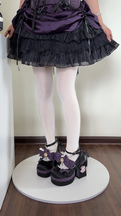 A person wearing a dark purple and black ruffled skirt, white tights, and black platform Mary Jane shoes with purple ribbon details, standing on a white circular platform in an indoor room.