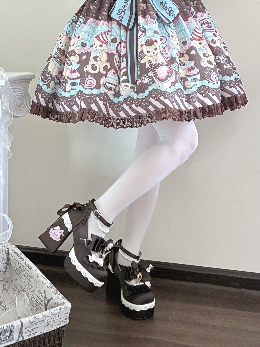 A person wearing a Lolita-style skirt with a teddy bear and dessert print, white tights, and black platform shoes with lace-up details, seated indoors on a wooden floor.