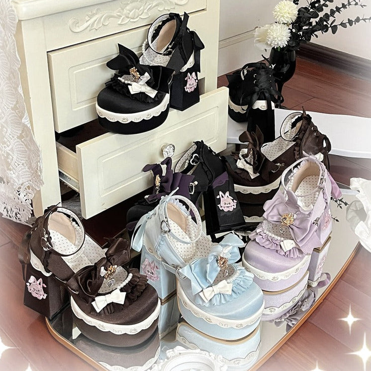 A collection of pastel Lolita-style platform shoes displayed on a mirrored tray and a small cream cabinet, featuring black, lavender, light blue, and pink designs with lace, bows, and decorative accents.