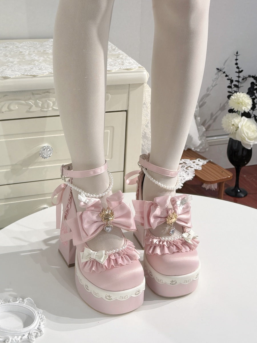 Pink platform Lolita shoes with large bows, pearl details, and ruffles, shown on a mannequin's feet in an indoor setting.