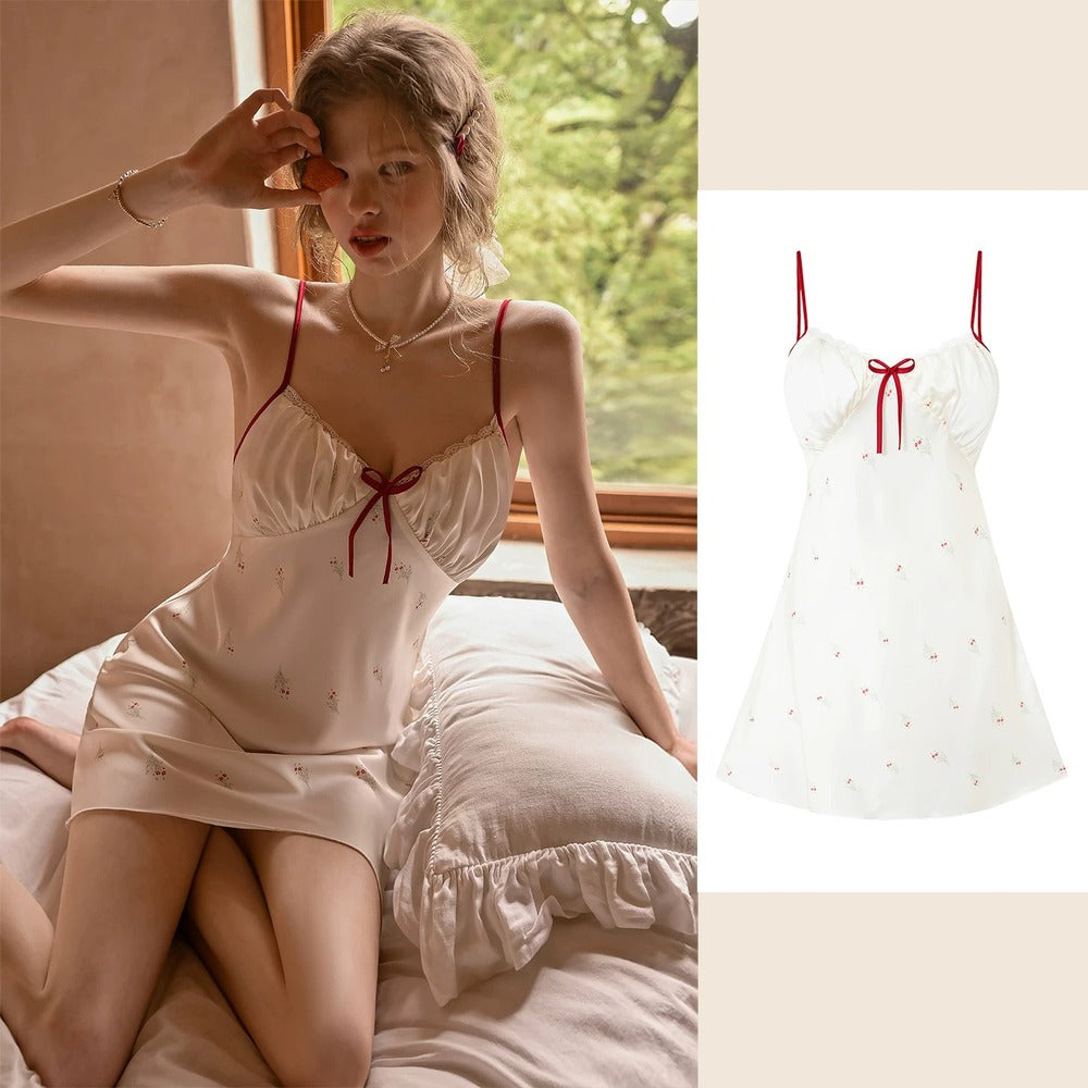 A woman wearing a short satin slip dress with red spaghetti straps and a red bow sits on a bed by a window, with a smaller product-only view of the dress on the right against a light beige background.