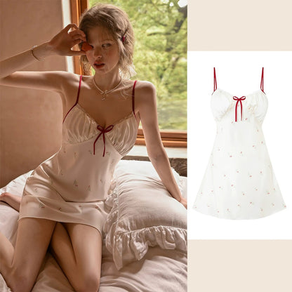 A woman wearing a short satin slip dress with red spaghetti straps and a red bow sits on a bed by a window, with a smaller product-only view of the dress on the right against a light beige background.