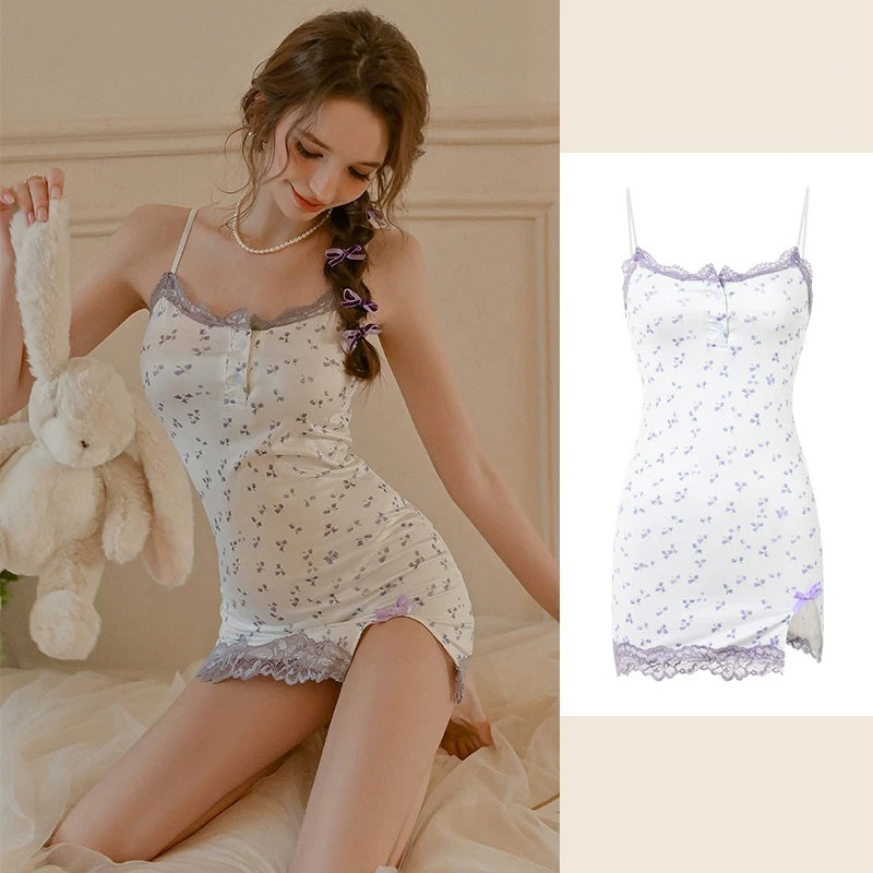 A woman wearing a white mini slip dress with a light purple floral print and lace trim, sitting on a bed and holding a plush bunny. A smaller inset on the right shows the dress alone against a light beige background.