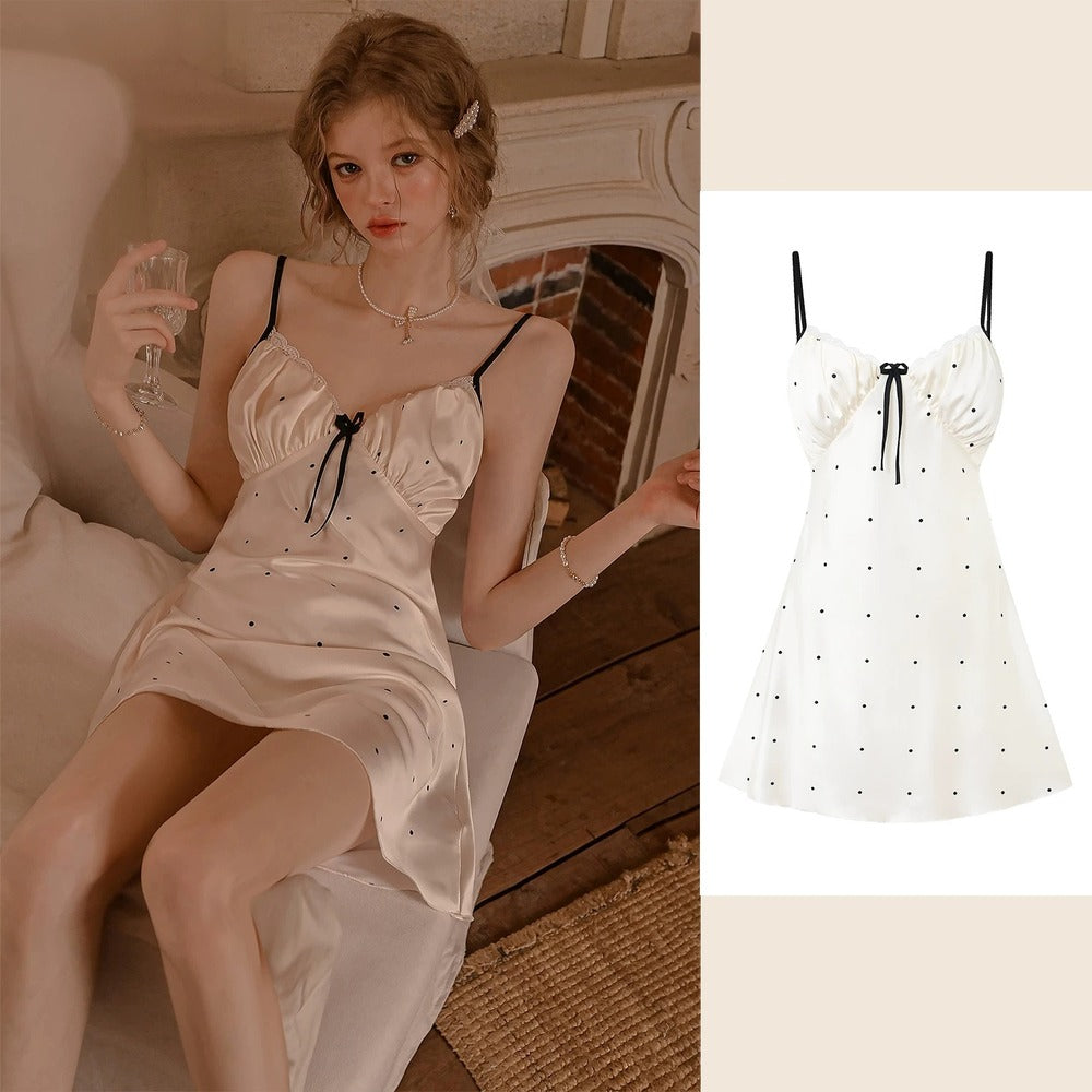 A woman wearing a satin slip dress with black polka dots and black spaghetti straps, sitting in a warm-toned room. The image is split, with the model on the left and a clean product shot of the dress on the right.