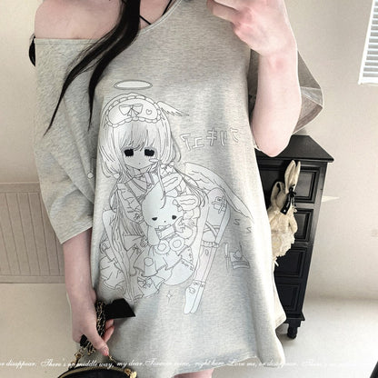 A person wearing an oversized light gray off-the-shoulder t-shirt with a white line-art anime graphic of a girl with angel wings and a rabbit character. The photo is taken in a room with a black cabinet in the background.