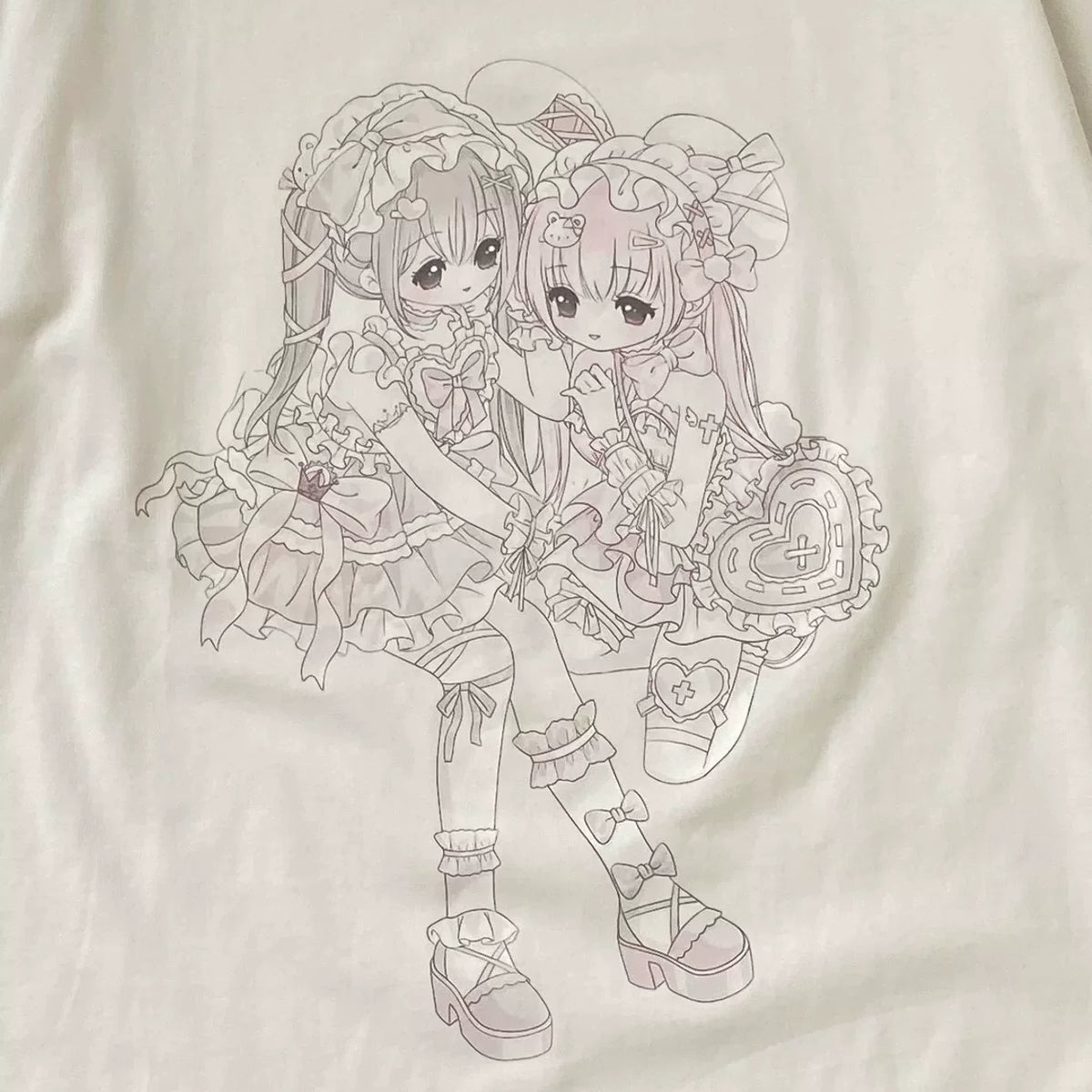 A close-up of a white T-shirt featuring a detailed line art graphic of two anime-style girls in elaborate lolita outfits, holding heart-shaped accessories.