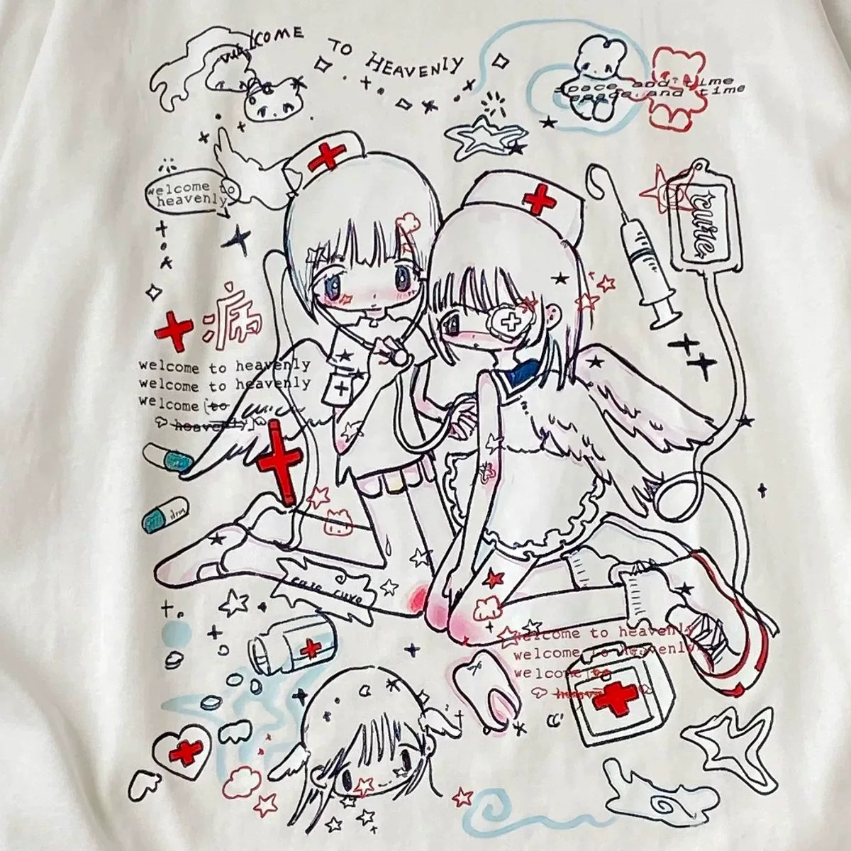 A close-up of a white graphic t-shirt featuring a detailed anime-style illustration of two angelic female characters dressed as nurses, surrounded by medical doodles, crosses, and text reading 'Welcome to Heaven'.