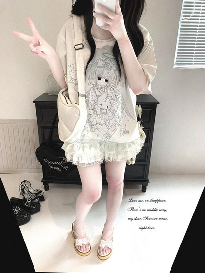 A person takes a mirror selfie showing a casual outfit consisting of a cream-colored graphic t-shirt with a black line art illustration, a matching oversized cream cardigan, a pleated cream mini skirt, and beige sandals. The setting is a mirror selfie in an indoor room with a black cabinet in the background.