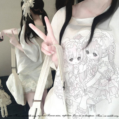 A close-up lifestyle shot of a person wearing a cream-colored oversized T-shirt with a detailed anime-style line art graphic of two chibi girls. The person is holding a matching cream shoulder bag and posing in front of a mirror that reflects the full outfit, which consists of a matching cream dress and a white bow headband.