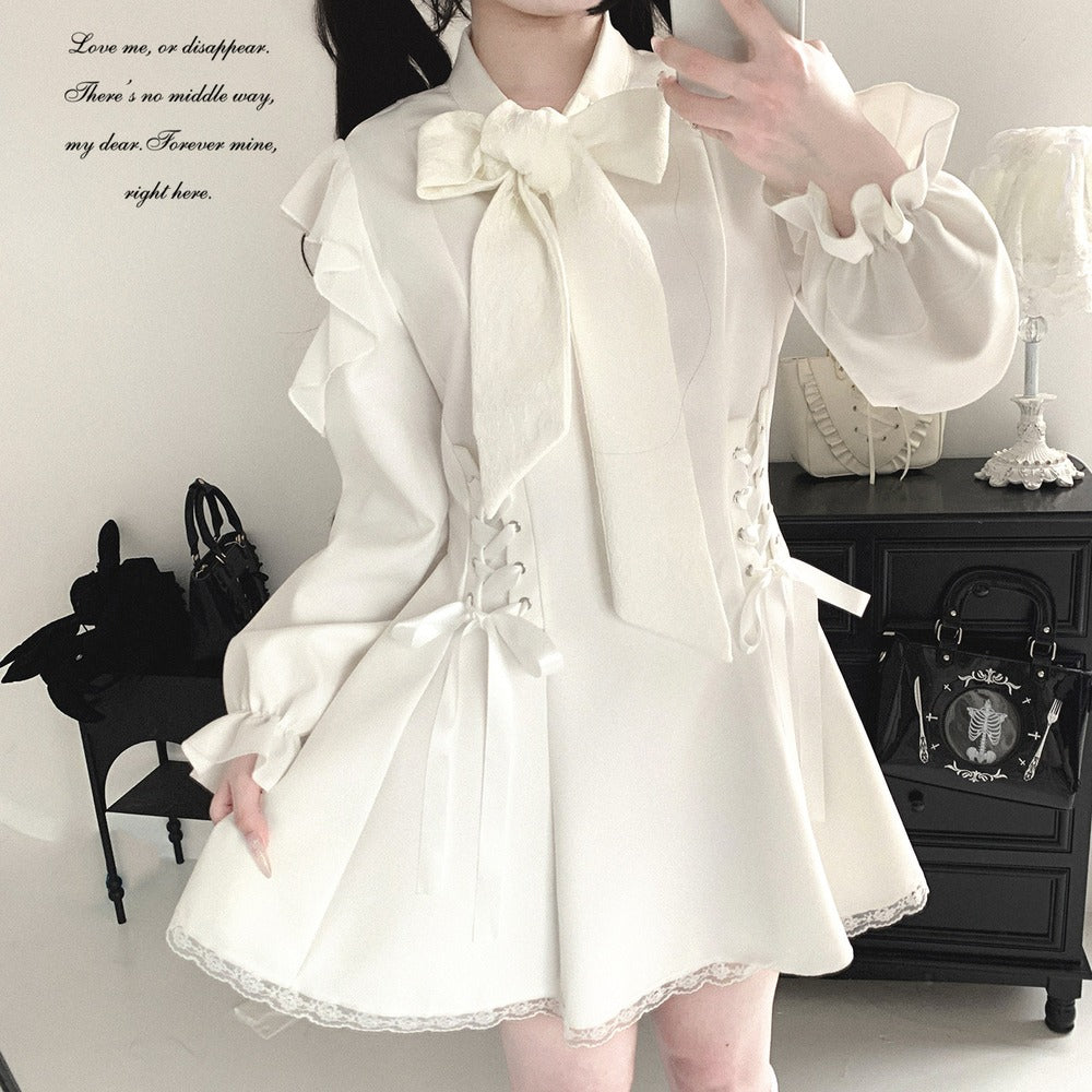 A person wearing a cream-colored Lolita-style long-sleeve blouse with a large bow at the collar, ruffled sleeves, lace-up side details, and a flared skirt with lace trim, shown in a mirror selfie in an indoor room.