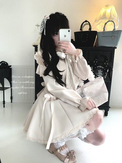 A person takes a mirror selfie wearing a cream-colored Lolita-style dress with lace details, ruffled sleeves, and a bow headband, holding a light pink clutch bag in a room with handbags on a black cabinet.