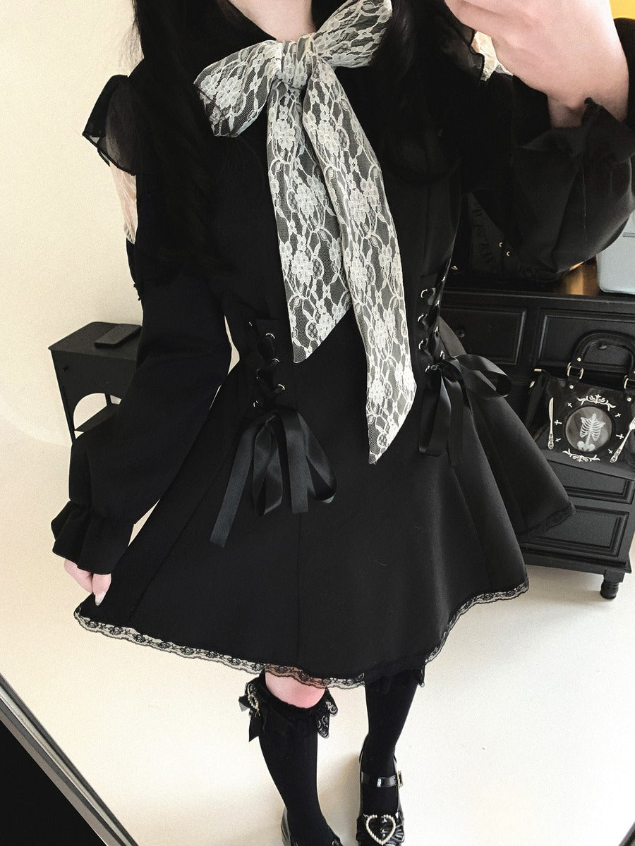 A person wearing a black Lolita-style dress with a large black and white snakeskin-patterned bow at the collar, black lace trim, side lacing, and black knee-high socks, photographed indoors in front of a mirror.