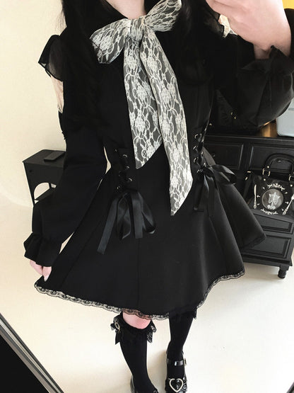 A person wearing a black Lolita-style dress with a large black and white snakeskin-patterned bow at the collar, black lace trim, side lacing, and black knee-high socks, photographed indoors in front of a mirror.