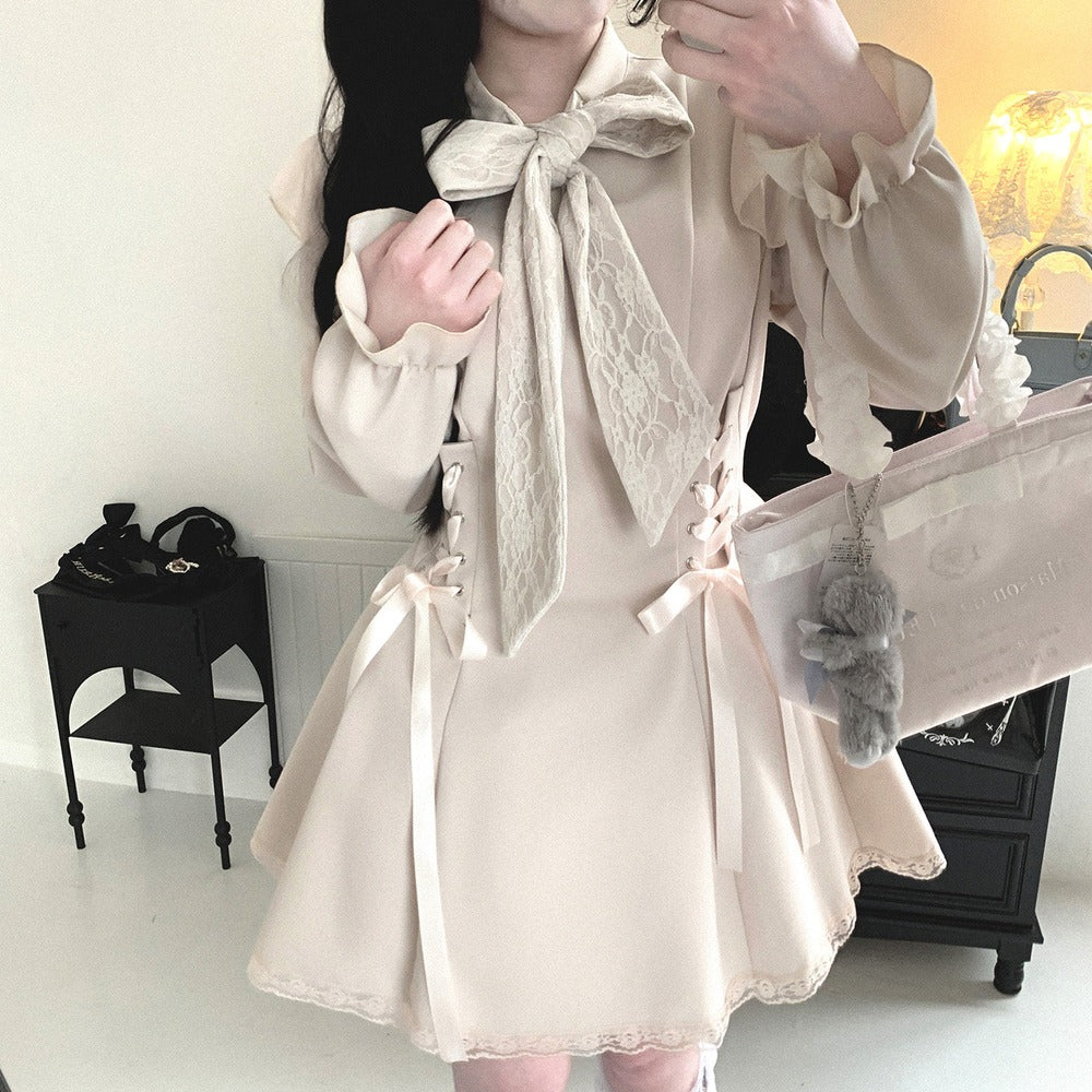 A person wearing a cream-colored Lolita-style dress with a large lace bow at the collar, ruffled sleeves, side lace-up corset details, and a flared skirt with lace trim. The person is holding a light pink tote bag with a gray plush keychain in an indoor room setting.