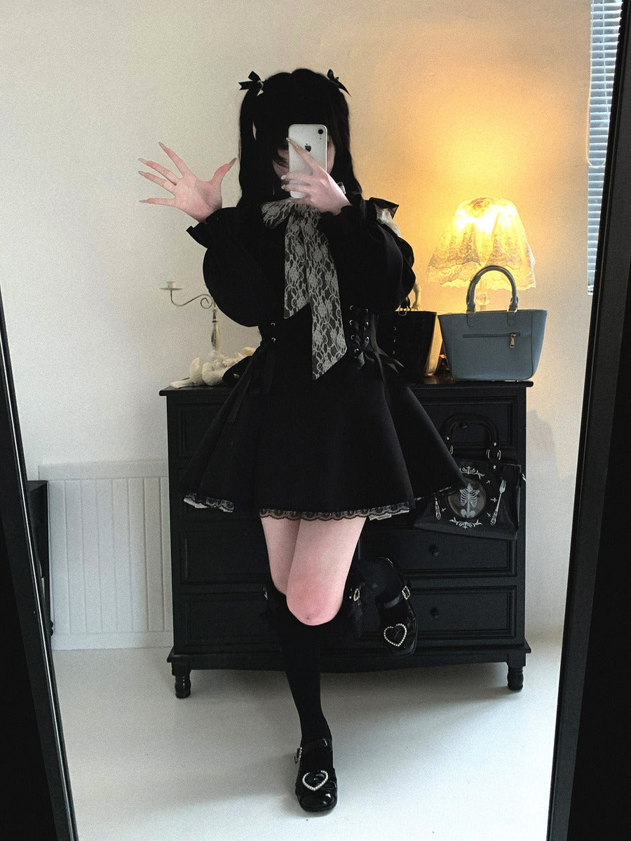 A person takes a mirror selfie wearing a black gothic Lolita-style outfit with a pleated skirt, lace-trimmed collar, black lace-up bow, and black thigh-high stockings in a room with a black dresser and warm lamp lighting.
