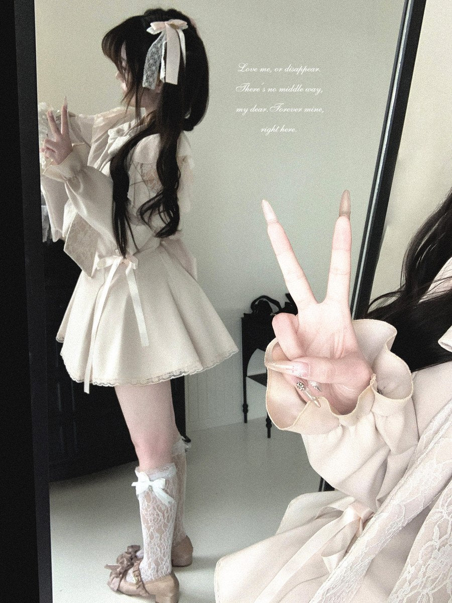 A woman wearing a cream-colored loli-style outfit with a pleated mini skirt, ruffled long sleeves, and lace knee socks, posing in front of a mirror that reflects her hand making a peace sign.