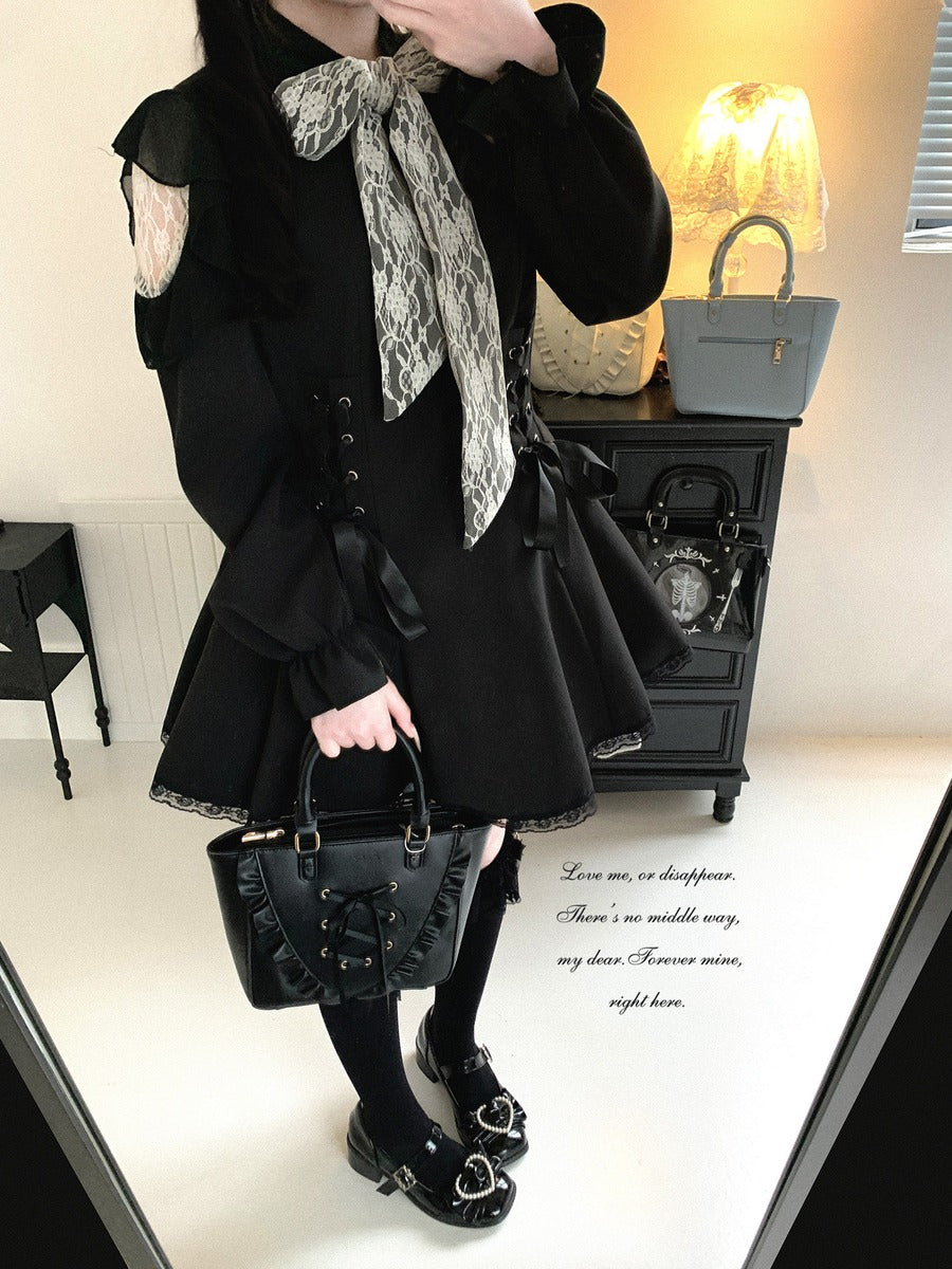 A person wearing a black Lolita-style dress with a large gray and white patterned bow at the collar, holding a black handbag in an indoor room setting.