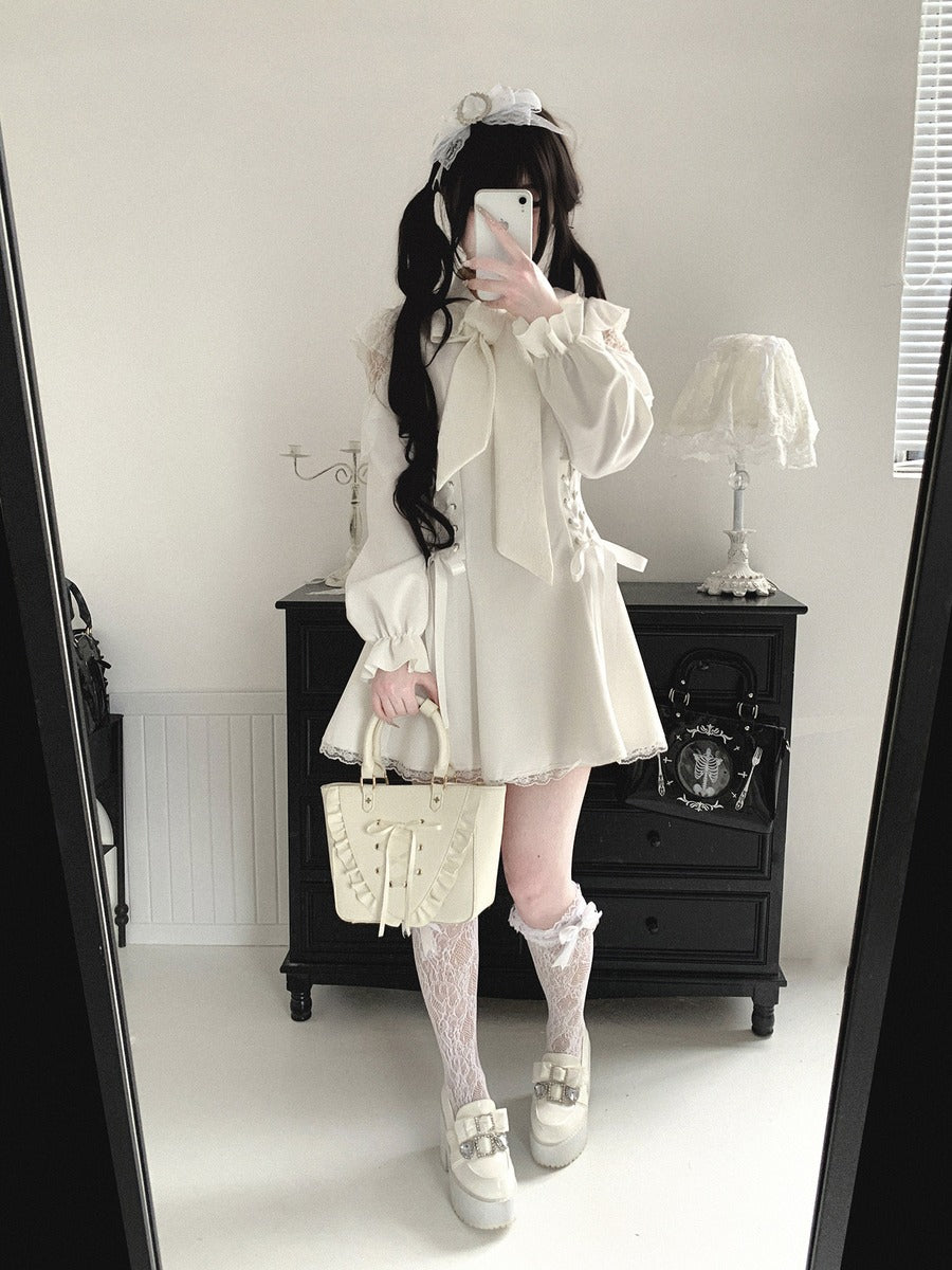 A person takes a mirror selfie in a room, wearing a cream-colored Lolita-style outfit consisting of a long-sleeve blouse with a large bow, a matching mini skirt, lace knee socks, and platform shoes. They are holding a cream-colored quilted handbag.