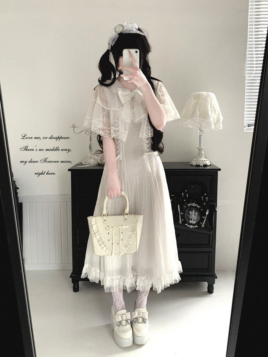Person wearing a white lace dress holding a beige handbag in a room with a black cabinet and white walls.