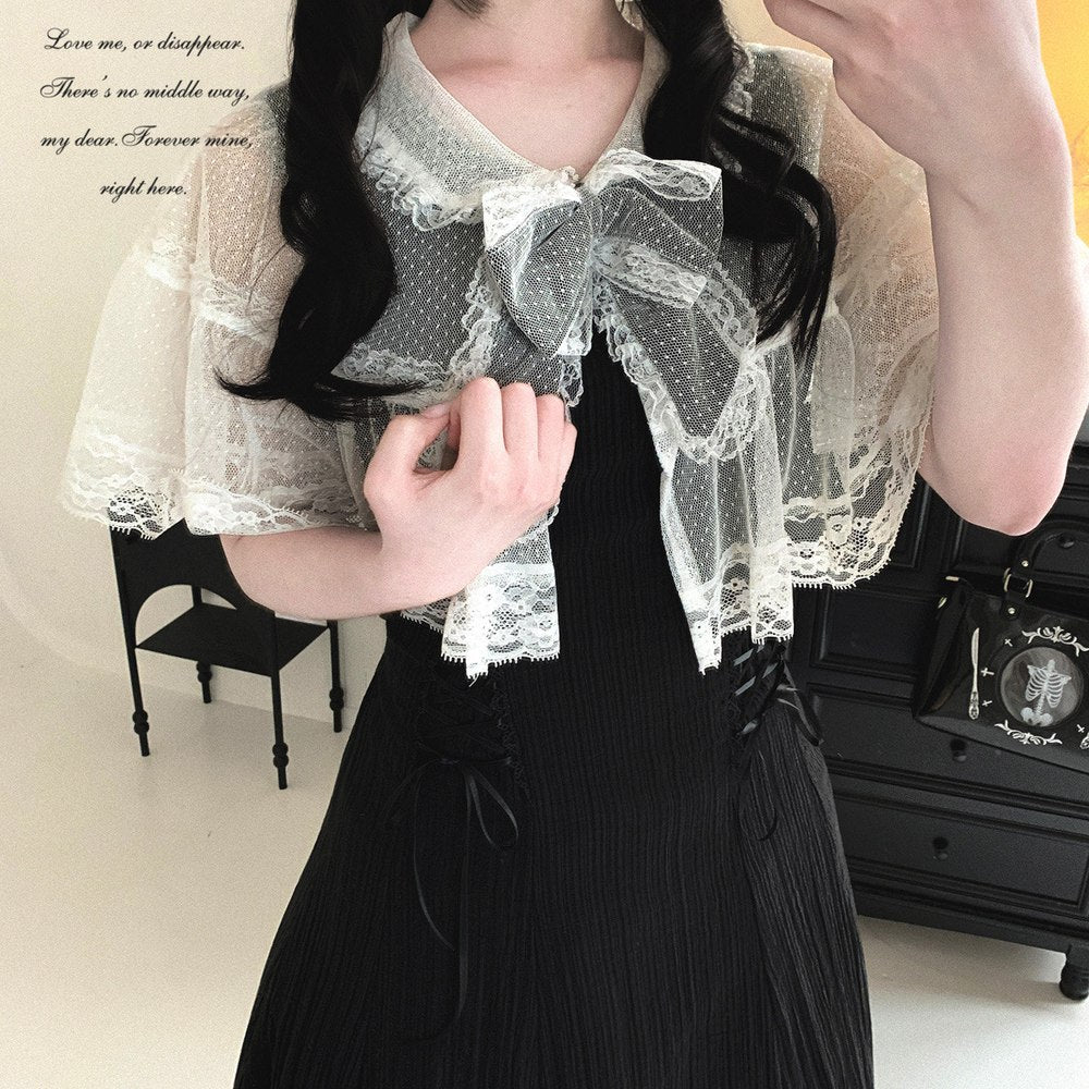 Person wearing a white lace blouse over a black dress with a vintage suitcase in the background.