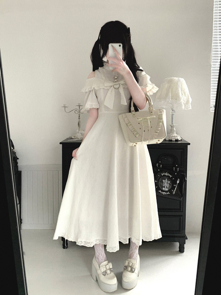 Person wearing a white dress with a lace top and skirt, holding a beige handbag in a room.