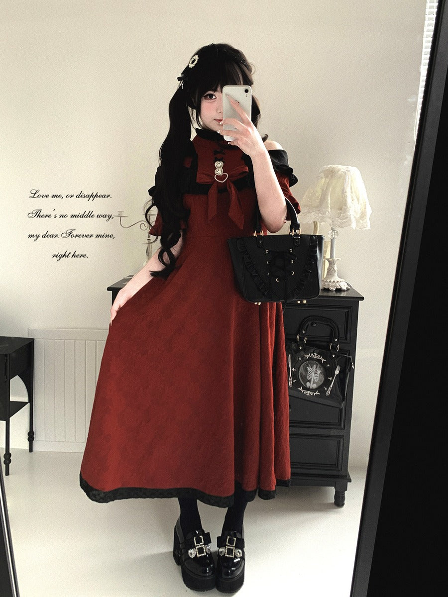 Person wearing a long red dress with a black top and skirt, holding a phone, in a room with a lamp and table.